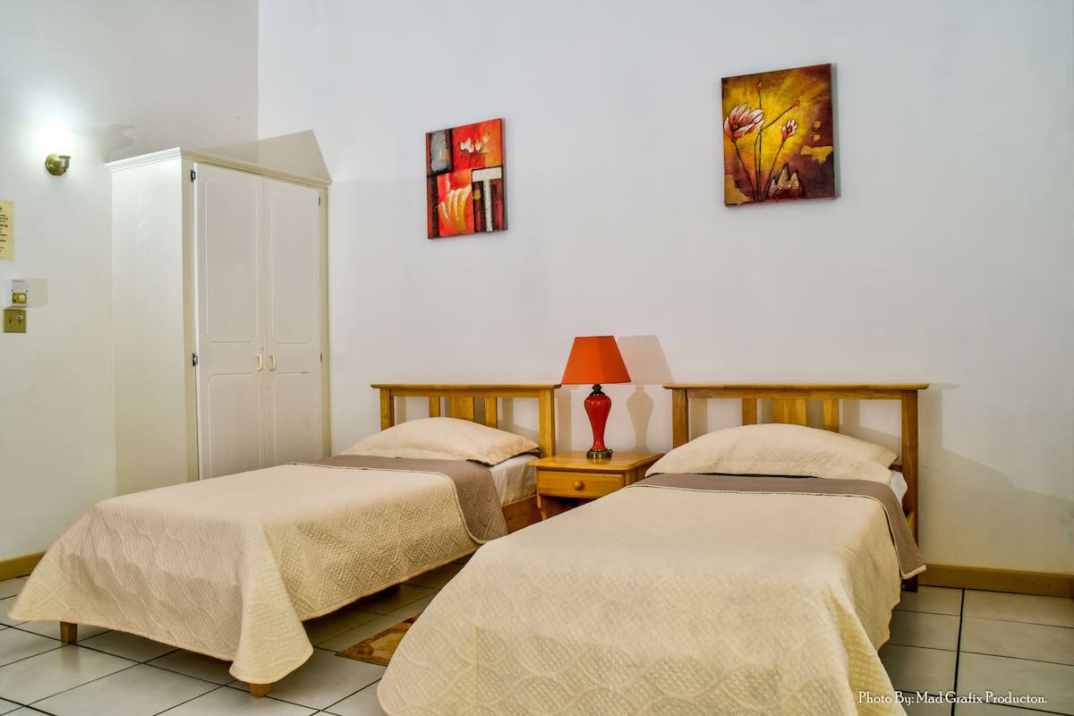 A room with two beds, a wardrobe, and two paintings on the wall.