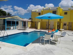 A swimming pool with lounge chairs and umbrellas, surrounded by yellow buildings. - Sun Fun Resort (Nassau)