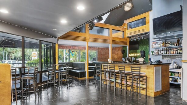 A modern bar area with seating and a bar counter, large windows, and a view of the outside. - Sun Fun Resort (Nassau)