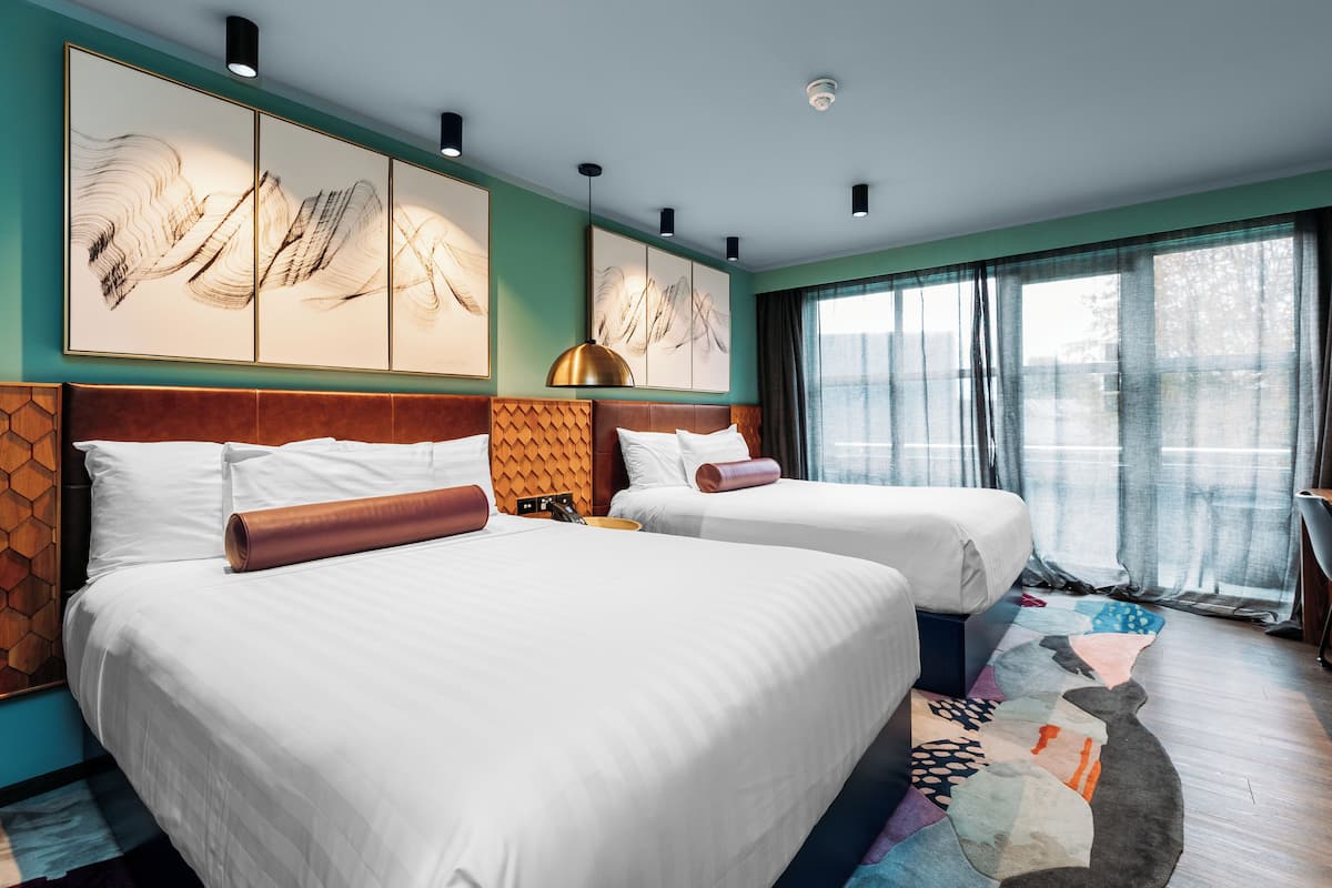 Een hotelkamer met twee bedden, een groot raam met gordijnen en kunstwerken aan de muur.