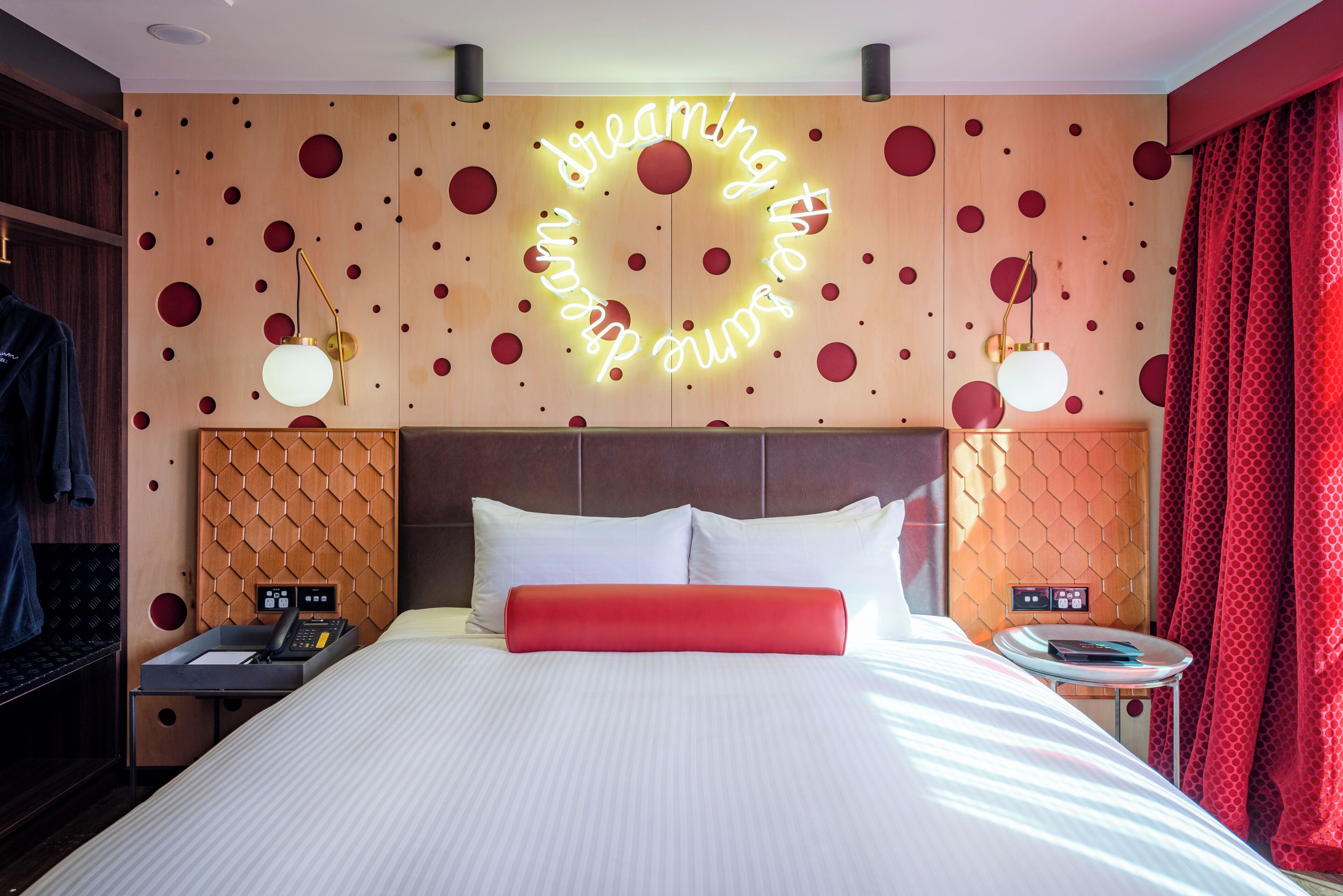 A hotel room with a large bed, a neon sign on the wall, and a red curtain.