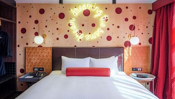 A hotel room with a large bed, a neon sign on the wall, and a red curtain.