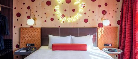A hotel room with a large bed, a neon sign on the wall, and a red curtain.