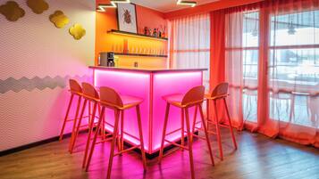 Eine Barbereich mit einer pink beleuchteten Theke und vier orangenen Stühlen.