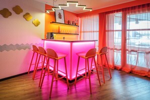 A bar area with a pink-lit bar counter and four orange chairs. - Naumi Hotel Auckland Airport (Auckland)