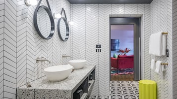 A modern bathroom with a herringbone tile pattern, two large white sinks, a mirror, and a yellow trash bin.