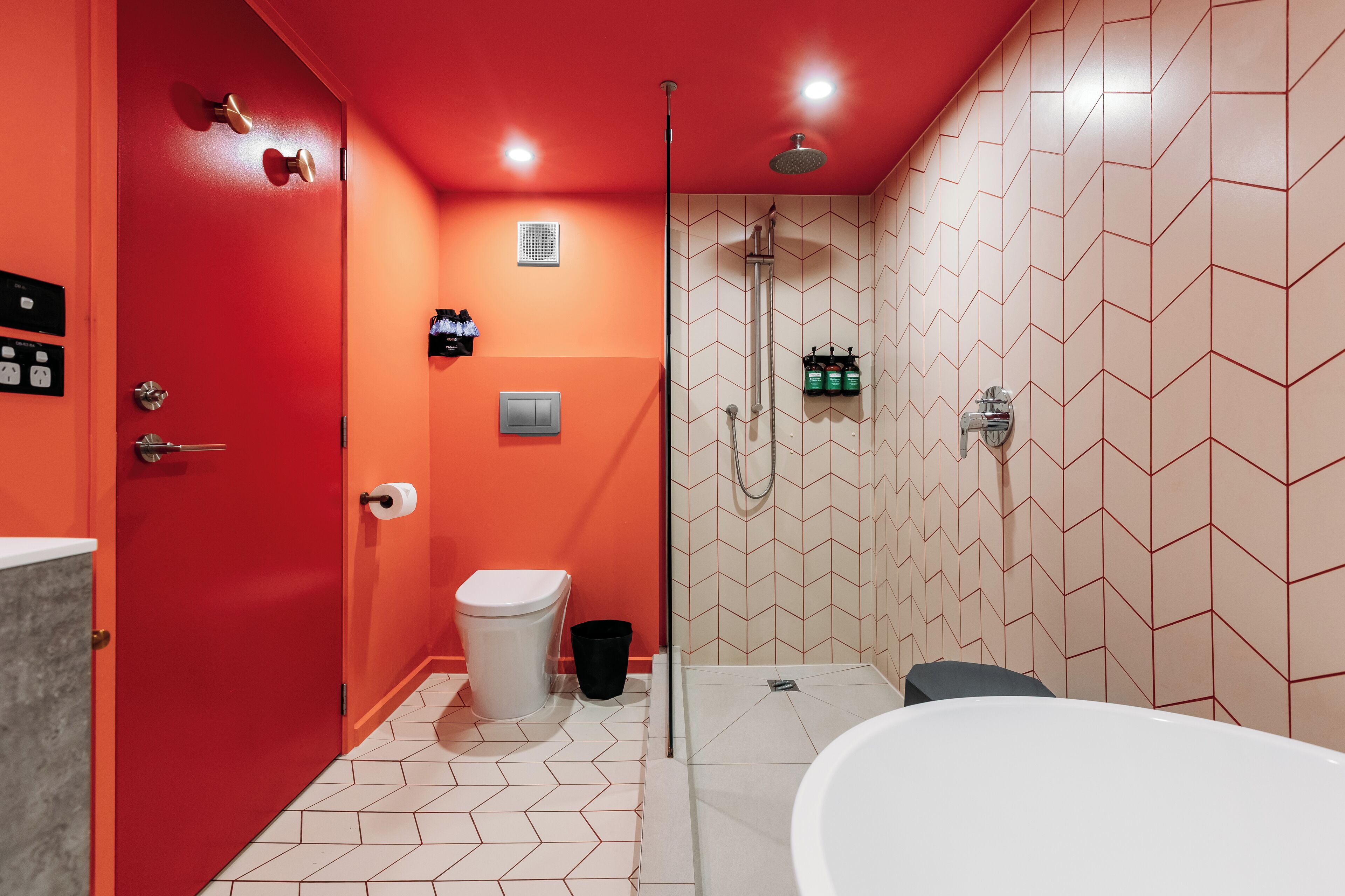Un baño con pared roja, inodoro blanco, zona de ducha y bañera.