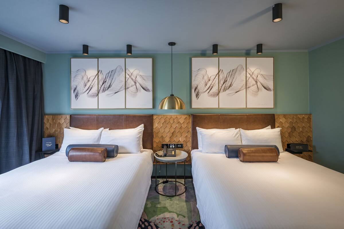 Une chambre d’hôtel avec deux lits, une table ronde, un téléphone et des œuvres d’art accrochées aux murs.