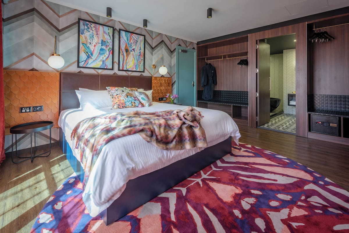 Een moderne hotelkamer met een groot bed, een bureau, een kledingkast en een badkamer zichtbaar door een geopende deur.