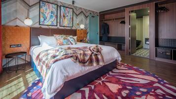 A modern hotel room with a large bed, a desk, a wardrobe, and a bathroom visible through an open door.