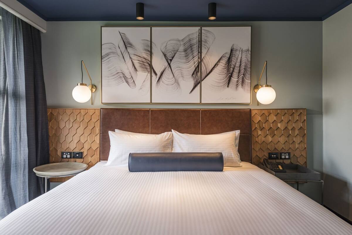 Een hotelkamer met een groot bed, twee nachtkastjes, een hoofdbord met een geometrisch patroon en een wanddecoratie.