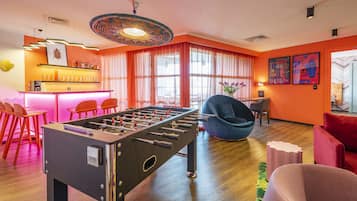 A brightly lit room with a foosball table, orange walls, and a bar area.