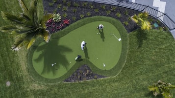 An aerial view of a golf course with a heart-shaped green, palm trees, and a curved walkway.