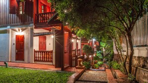 Une maison traditionnelle en bois, dotée d’un balcon, d’un petit jardin et d’un chemin menant à l’entrée.