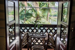 Een balkon met een tafel en stoelen, een bloempot en uitzicht op palmbomen.