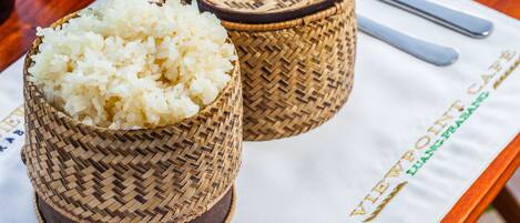 Two woven bamboo containers filled with white rice, placed on a table with a placemat that has the text "VIEWPOINT LUANG PRABONG" and a pair of silver utensils.