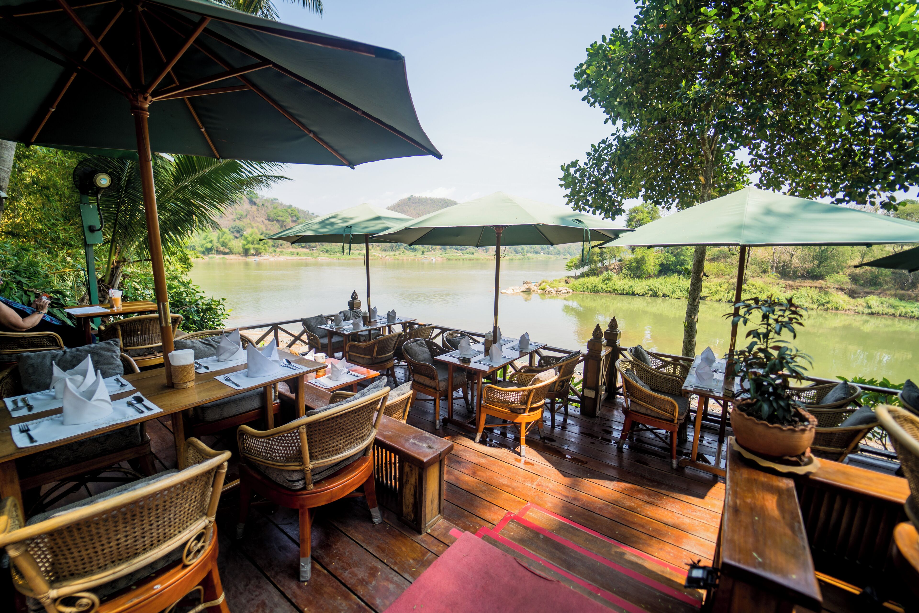 A wooden deck with tables and chairs, umbrellas, and a view of a river.