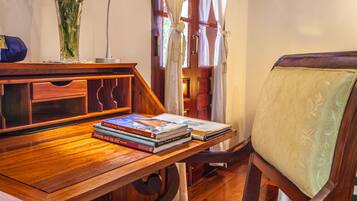 A wooden desk with books and a vase, a wooden chair with a cushioned seat, and a door with curtains.