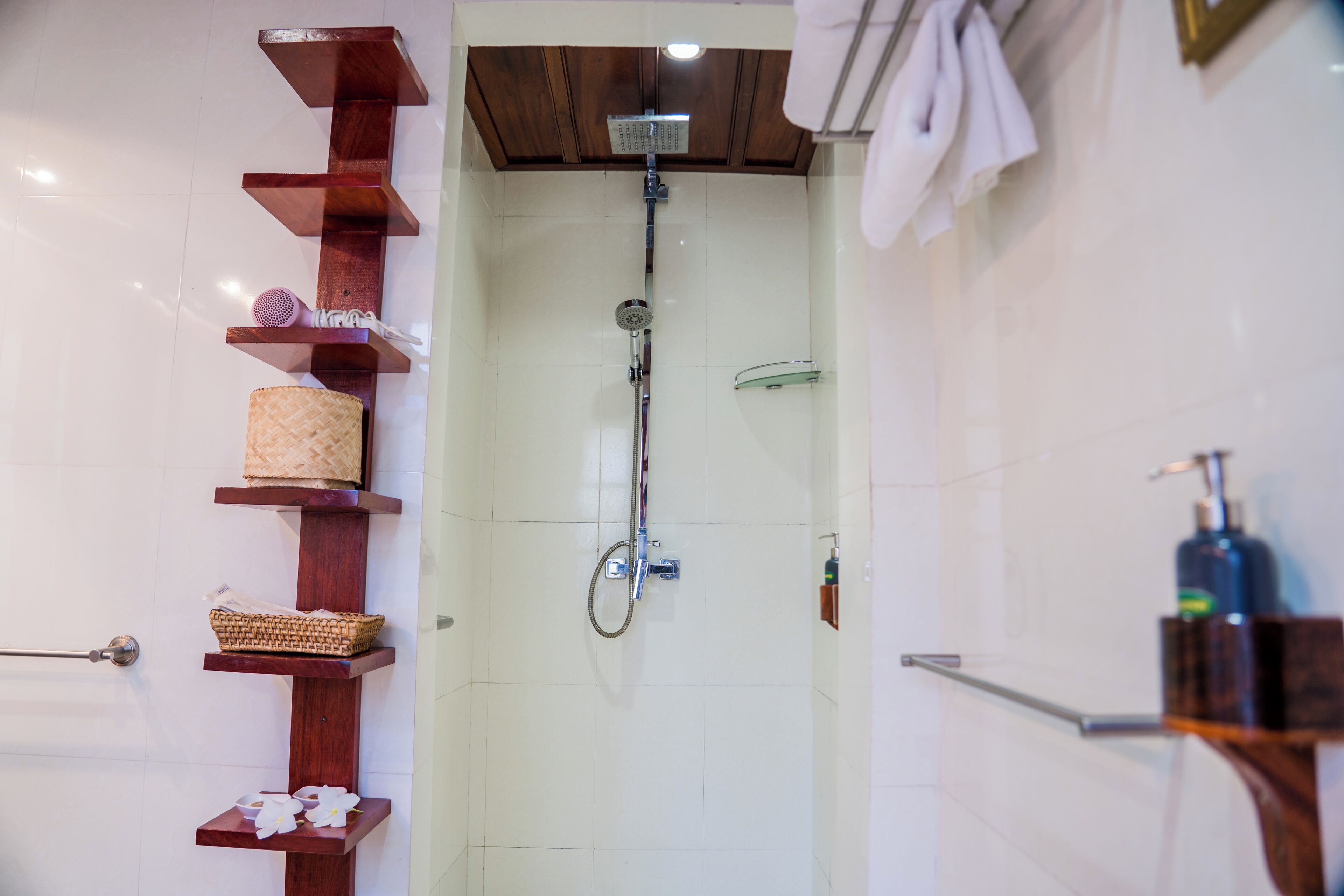 A shower with a wooden shelf holding a basket, a bottle, and a container.