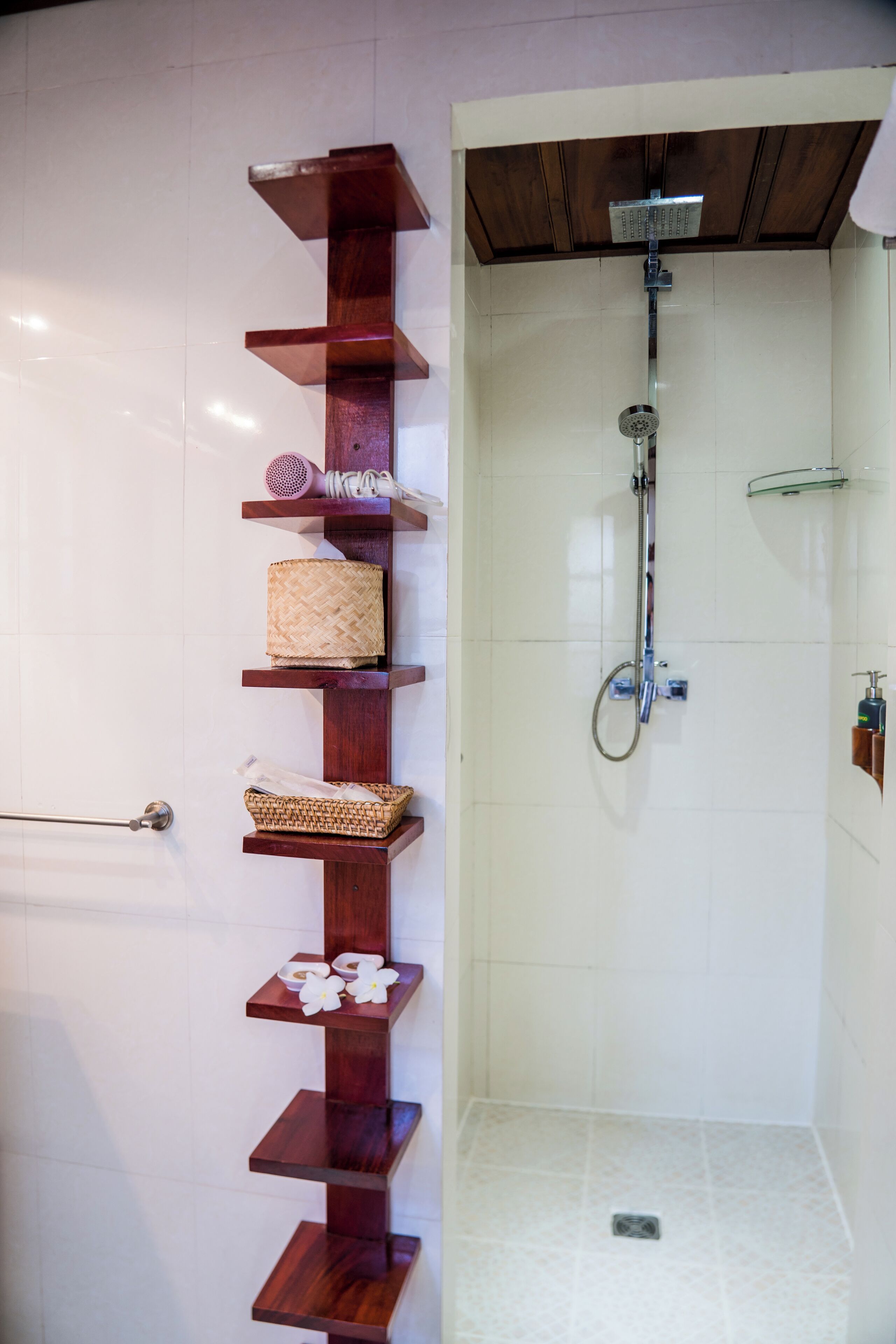 A shower area with a wooden shelf holding toiletries and a glass shelf above.