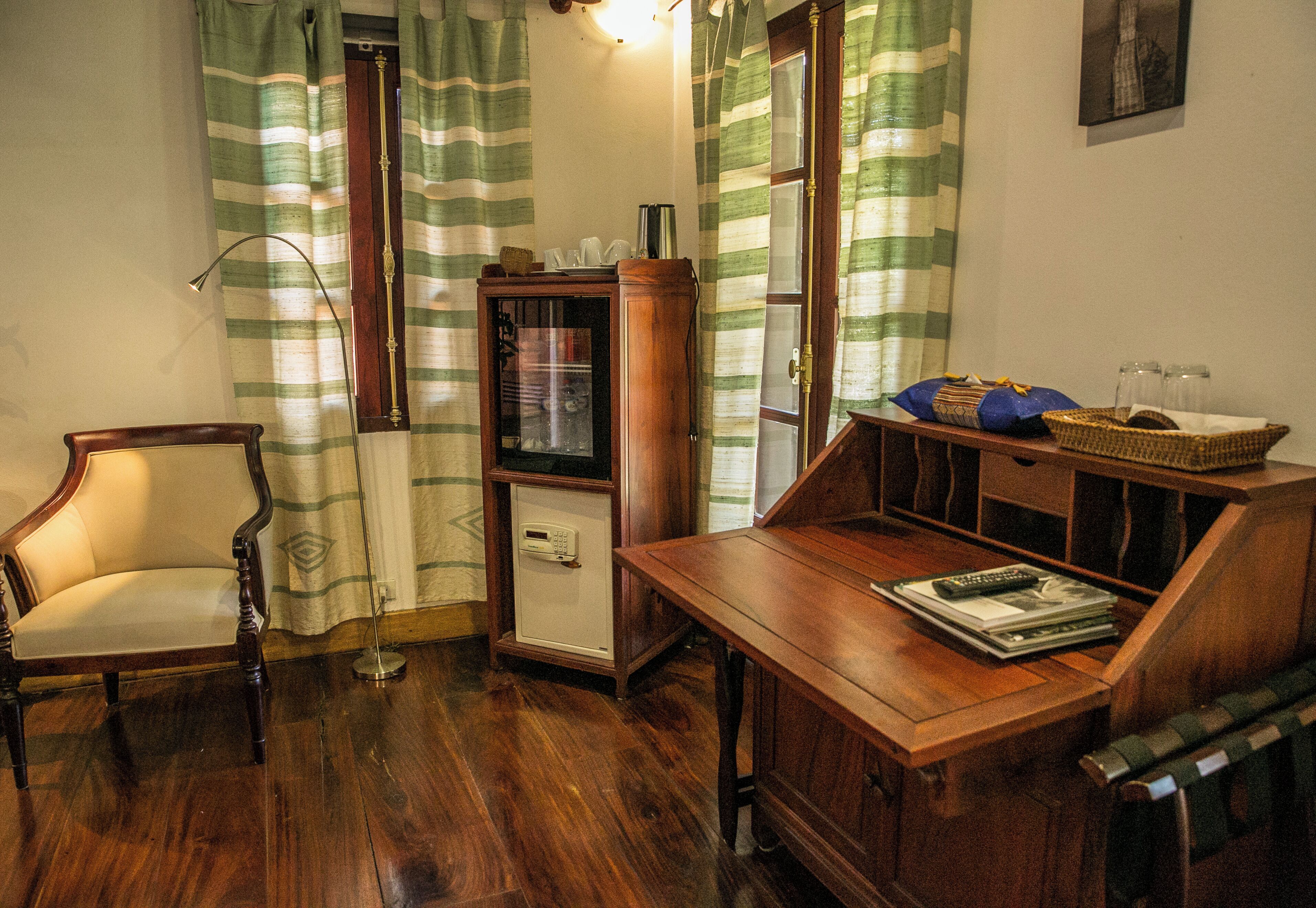 Une pièce comprenant une chaise en bois, un petit meuble, une table en bois et une fenêtre ornée de rideaux à rayures.