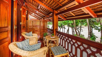 A wooden balcony with wicker furniture, a view of palm trees, and a wooden lattice partition.