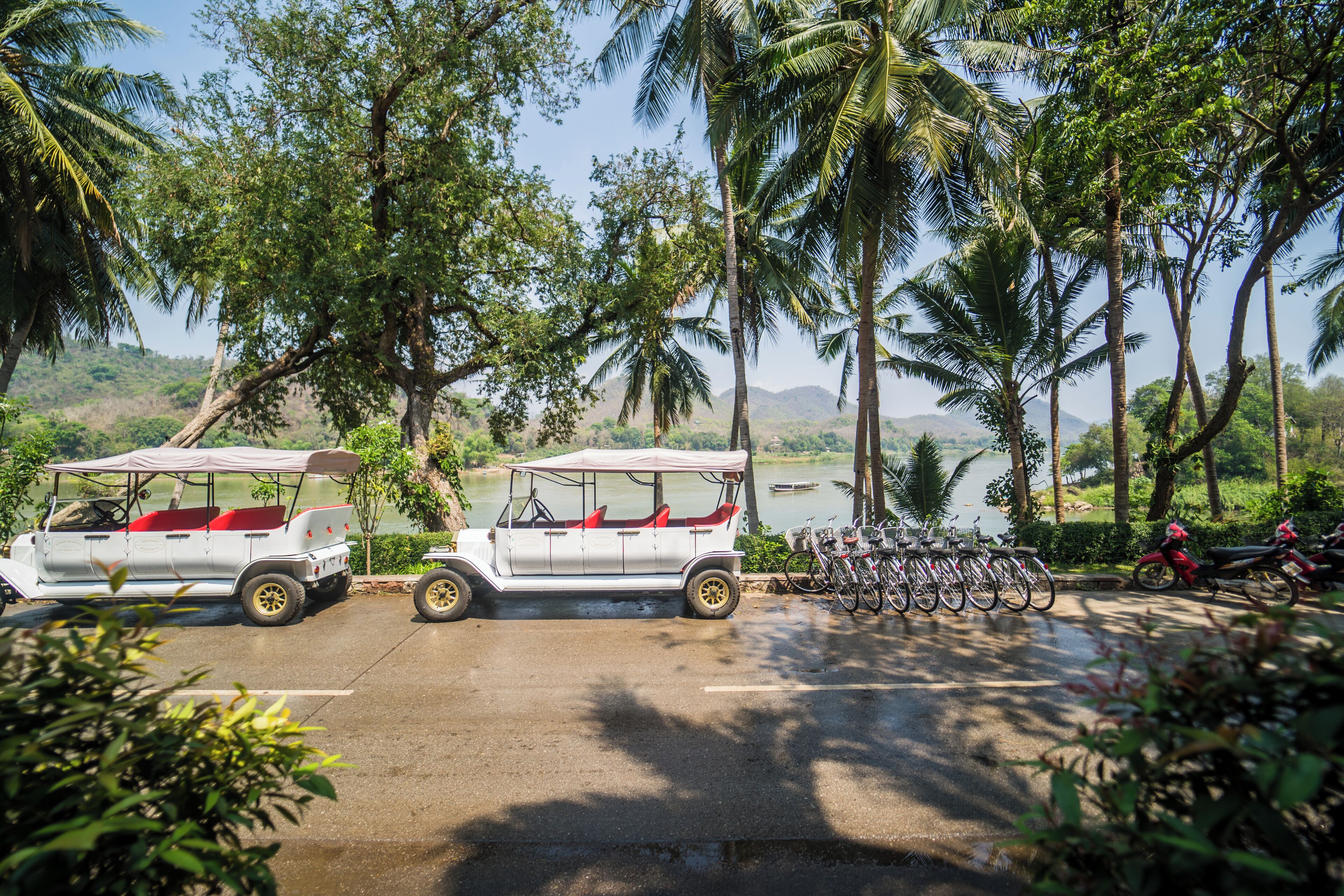 A white vehicle with red seats parked in a lot with bicycles and a water body in the background.