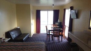 Ein Hotelzimmer mit Bett, Sofa, Esstisch mit Stühlen, Fernseher und Blick ins Freie.