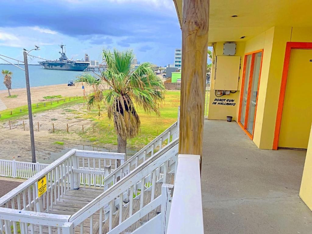 A balcony with a view of a beach and a ship, a wooden railing, and a door with a sign.