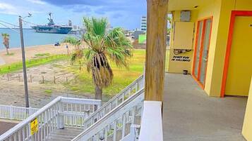 A balcony with a view of a beach and a ship, a wooden railing, and a door with a sign.