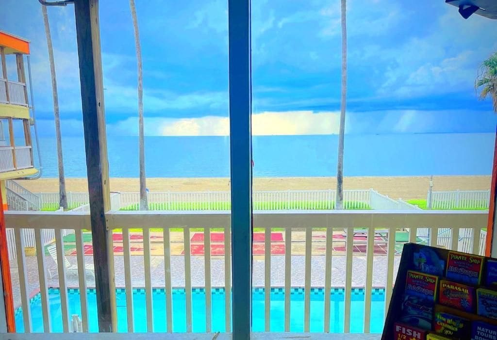 Zona de piscina con vista a la playa y al océano, un puesto de socorristas y un cartel con texto.