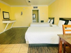 A hotel room with two beds, a small table, a chair, and a bathroom visible through an open door.