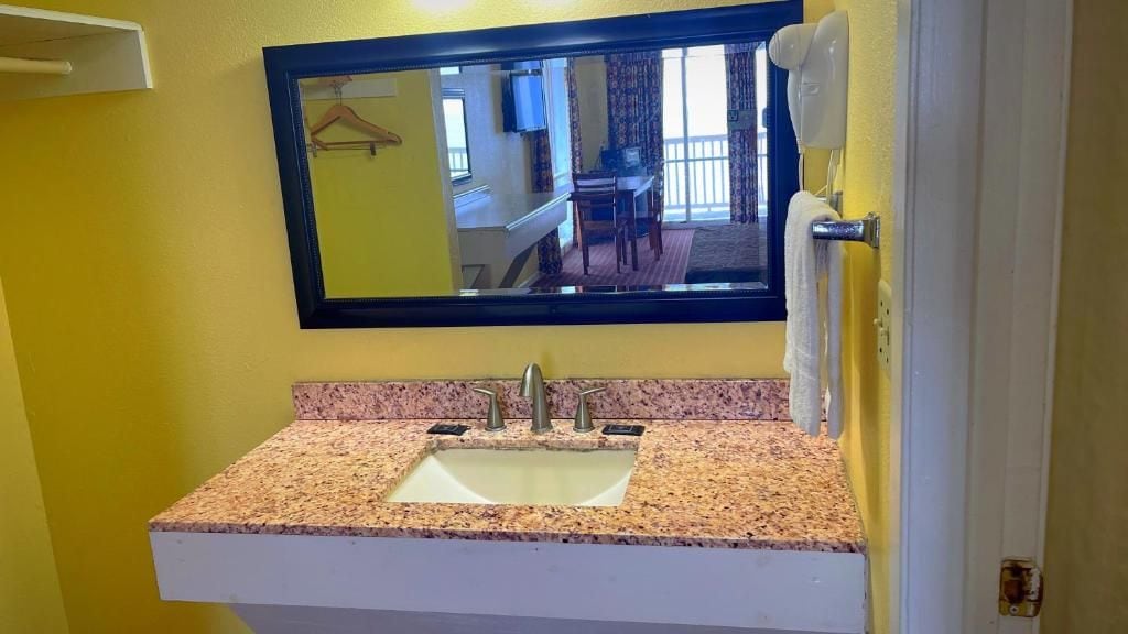 A bathroom with a granite countertop sink, a mirror above it, and a towel rack to the right.