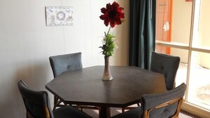 Ein runder Tisch mit vier Stühlen, einer Vase mit einer roten Blume und einem gerahmten Bild an der Wand.