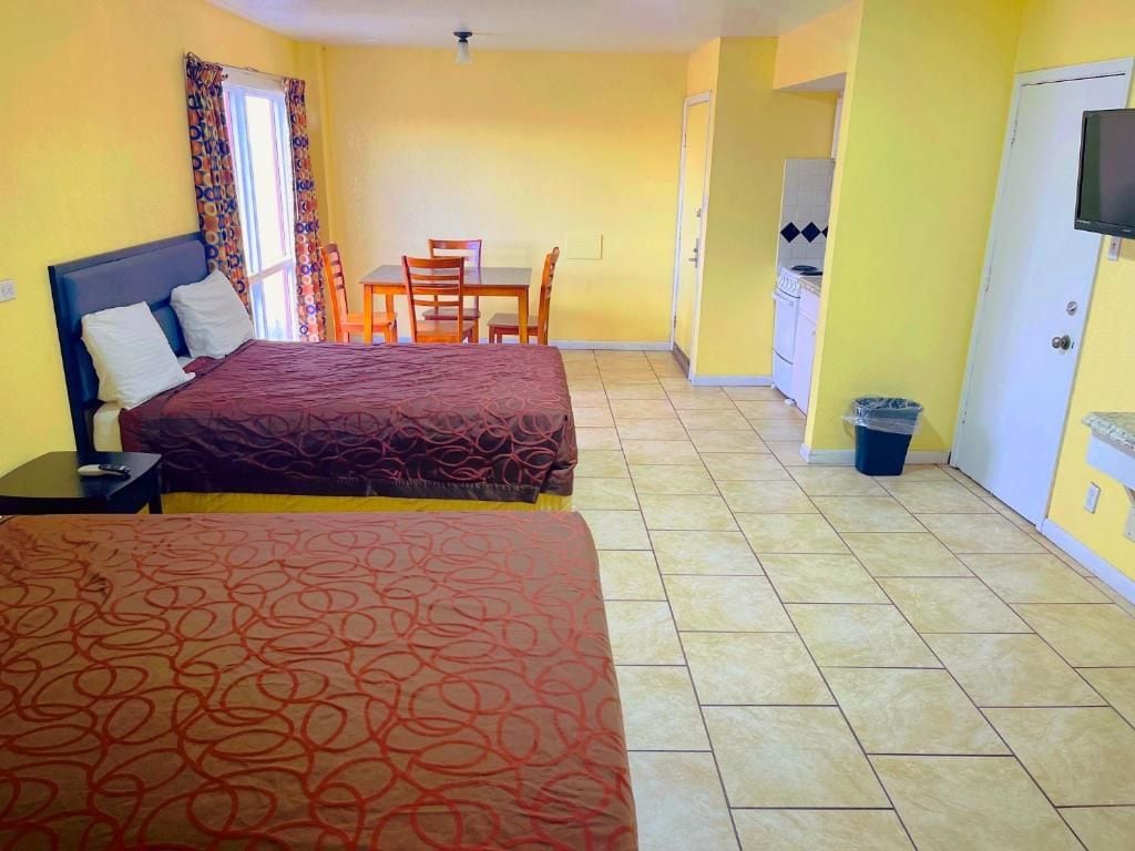 A room with two beds, a dining table, chairs, a TV, and a kitchenette.
