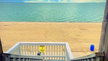 Vista de la playa con un letrero de precaución en una barandilla de madera.