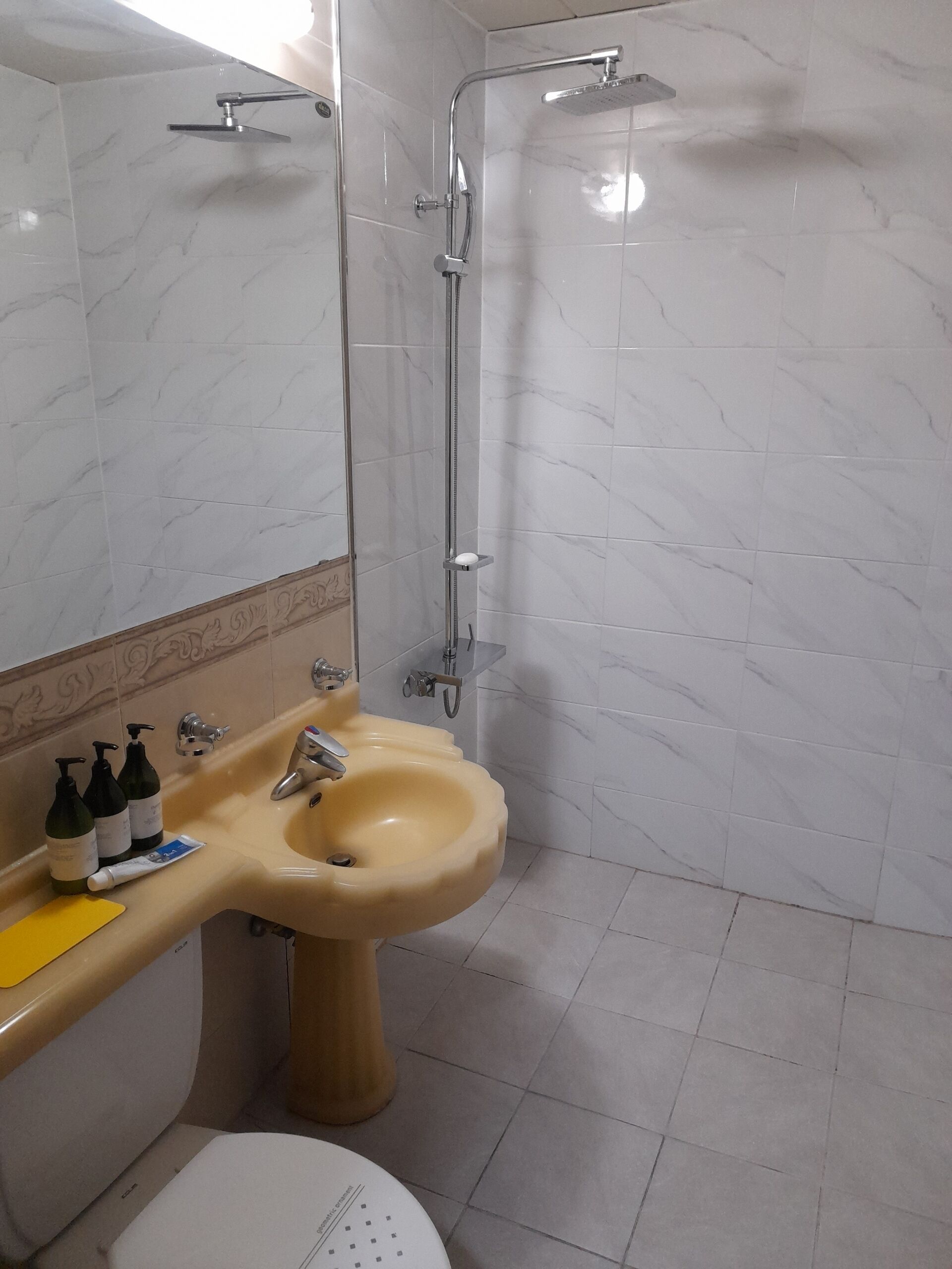 Un baño con ducha de azulejos de mármol, un lavamanos color beige y un inodoro.