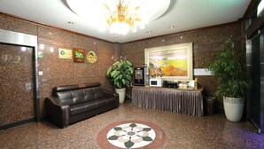 A lobby with a brown leather sofa, a coffee station, a large potted plant, and a painting on the wall. - Suncheon Noblesse Hotel (Suncheon)