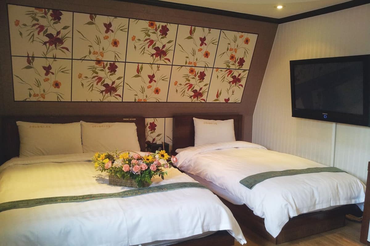 A hotel room with two beds, a floral headboard, a flat-screen TV, and a floral arrangement on the bed.
