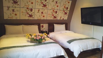 Habitación de hotel con dos camas, cabecera estampada con motivos florales, televisión de pantalla plana y un arreglo floral sobre la cama.