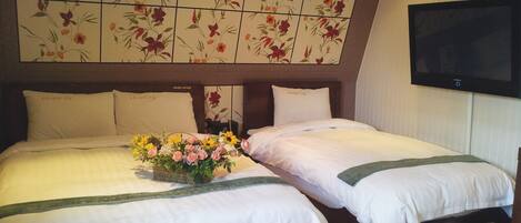 Habitación de hotel con dos camas, cabecera estampada con motivos florales, televisión de pantalla plana y un arreglo floral sobre la cama.