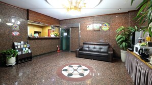 A lobby with a reception desk, a black leather sofa, a chandelier, and a patterned floor design. - Suncheon Noblesse Hotel (Suncheon)