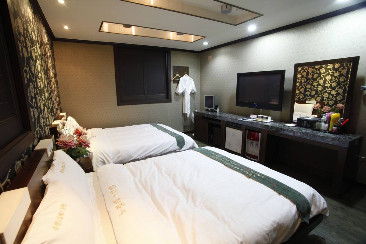 A hotel room with two beds, a desk with a flat-screen TV, a mirror, and a small TV on the desk.