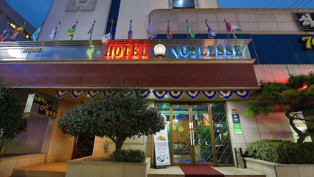 A hotel entrance with a sign reading "HOTEL NOBLESSE" and multiple flags displayed above. - Suncheon Noblesse Hotel (Suncheon)