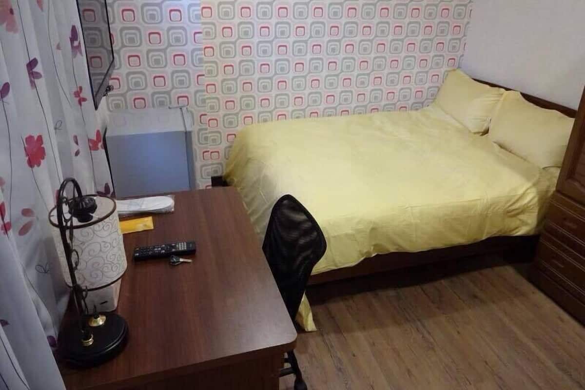 A bedroom with a wooden desk, a bed with yellow bedding, and a patterned wall.