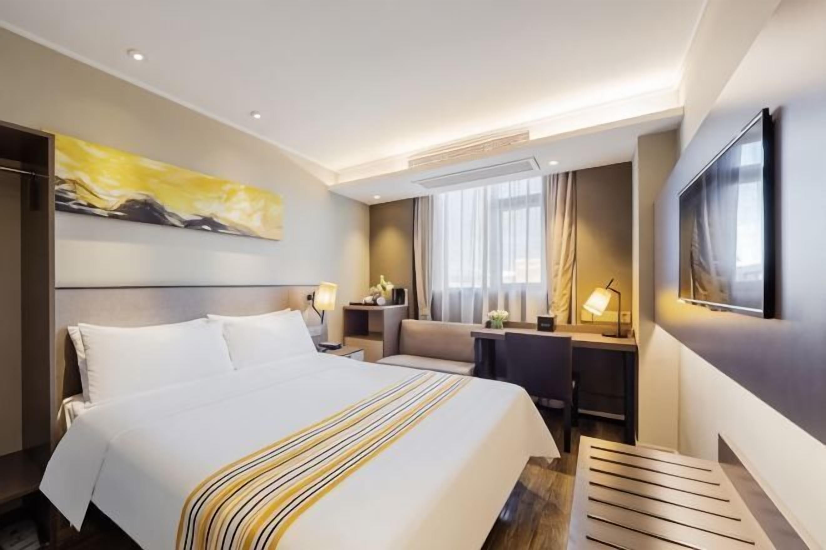 A hotel room with a large bed, a desk, a chair, a TV, and a painting on the wall.