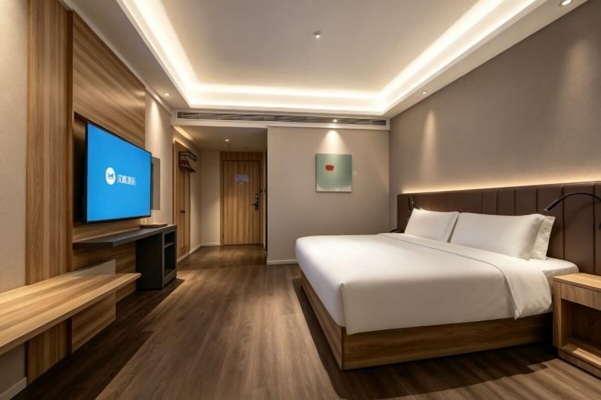 Una habitación de hotel con una cama, un televisor, un banco y una puerta.