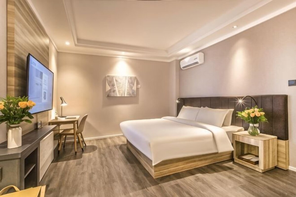 Habitación de hotel moderna con cama, mesita de noche, escritorio, silla y televisor.
