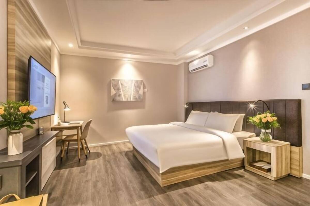 Une chambre d’hôtel moderne équipée d’un lit, d’une table de chevet, d’un bureau, d’une chaise et d’un téléviseur.