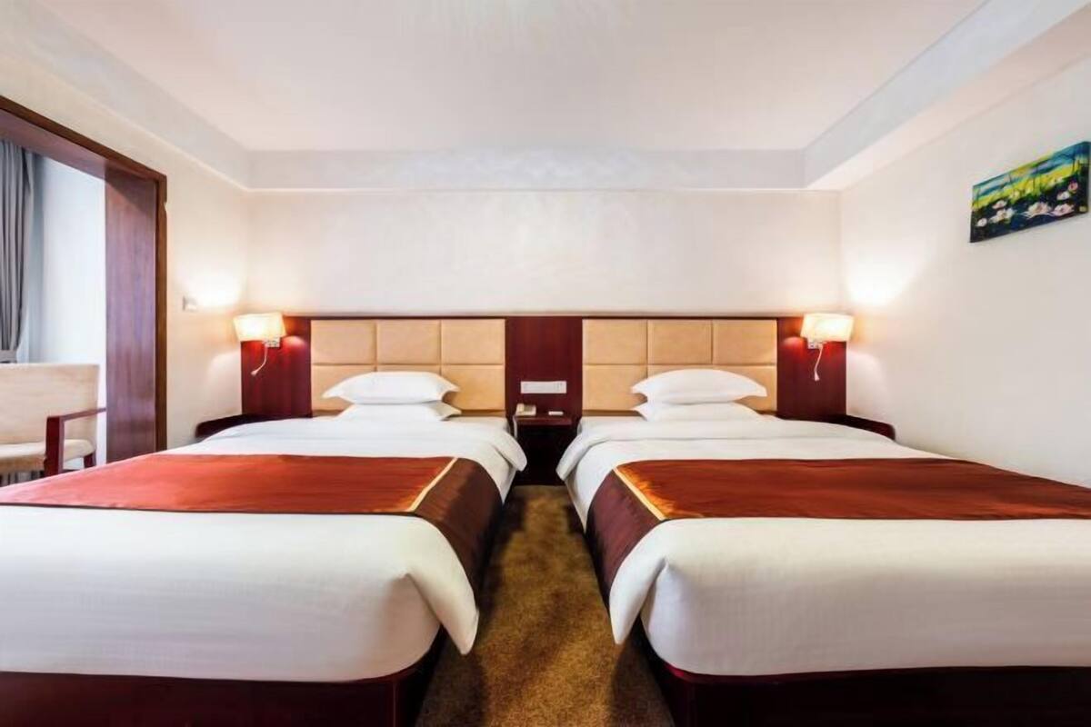 Habitación de hotel con dos camas, cabecera, lámparas de noche, suelo alfombrado y un cuadro en la pared.